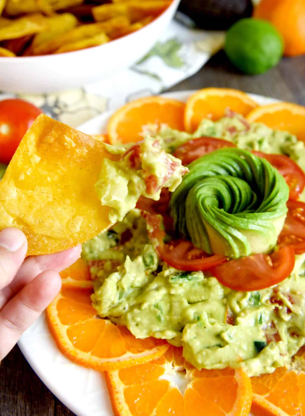 Guacamole platter with chips on a platter with decorative avocado rose, tomatoes and citrus. 